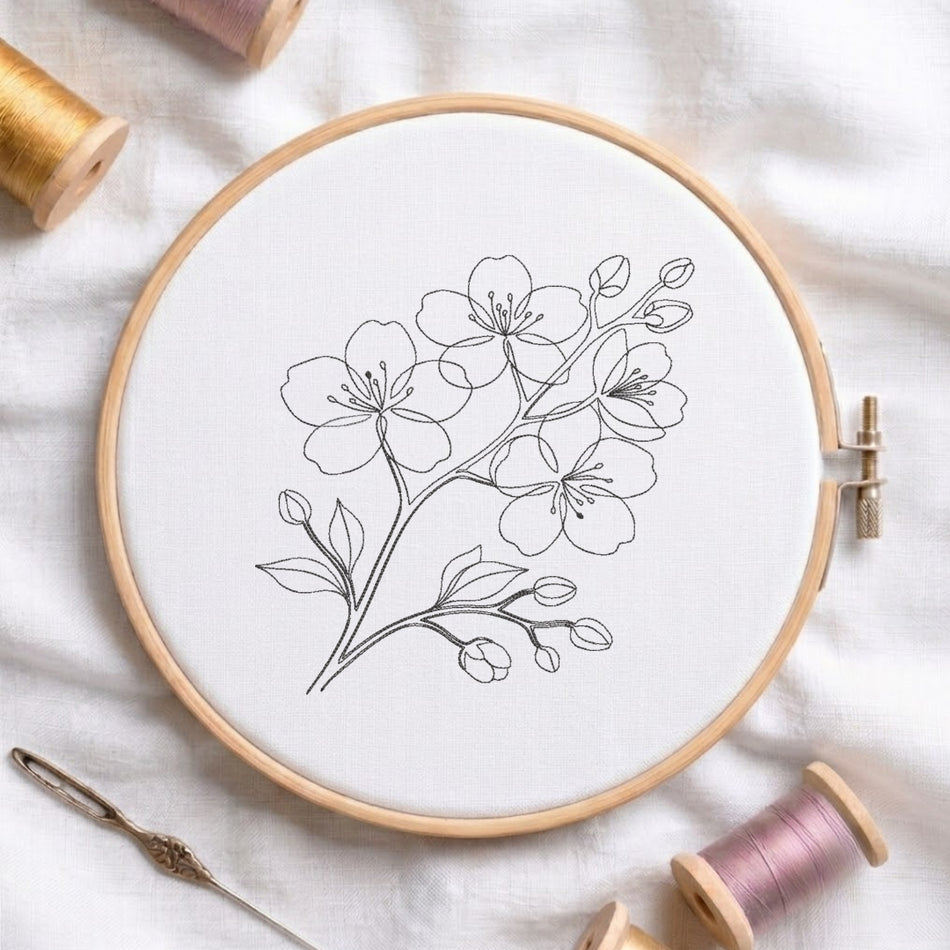 A black continuous line art cherry blossom branch machine embroidery design stitched on white fabric inside a wooden embroidery hoop, surrounded by thread spools.