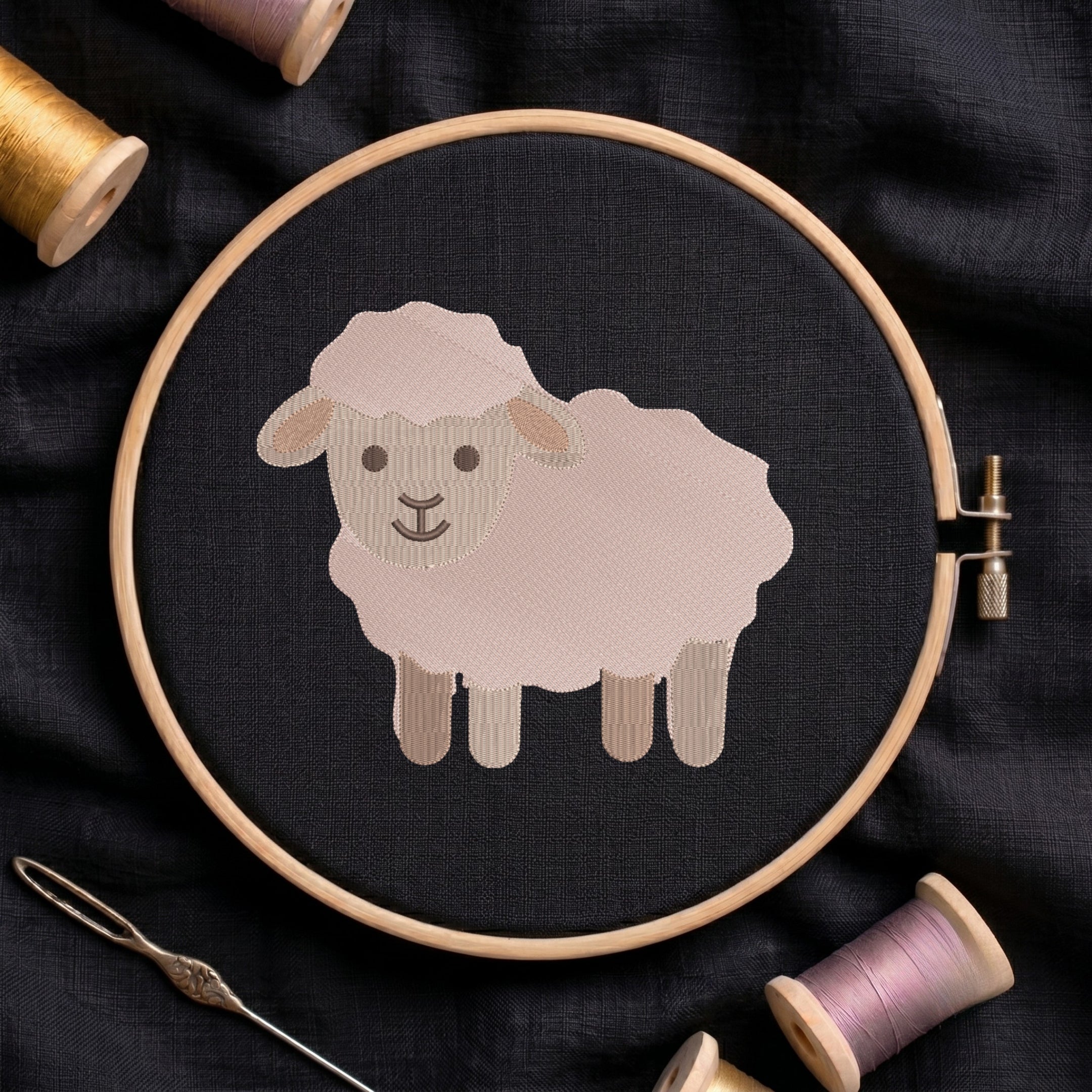 A circular embroidery hoop holding a stitched sheep design on dark fabric, surrounded by spools of thread and a needle on a dark textile background.