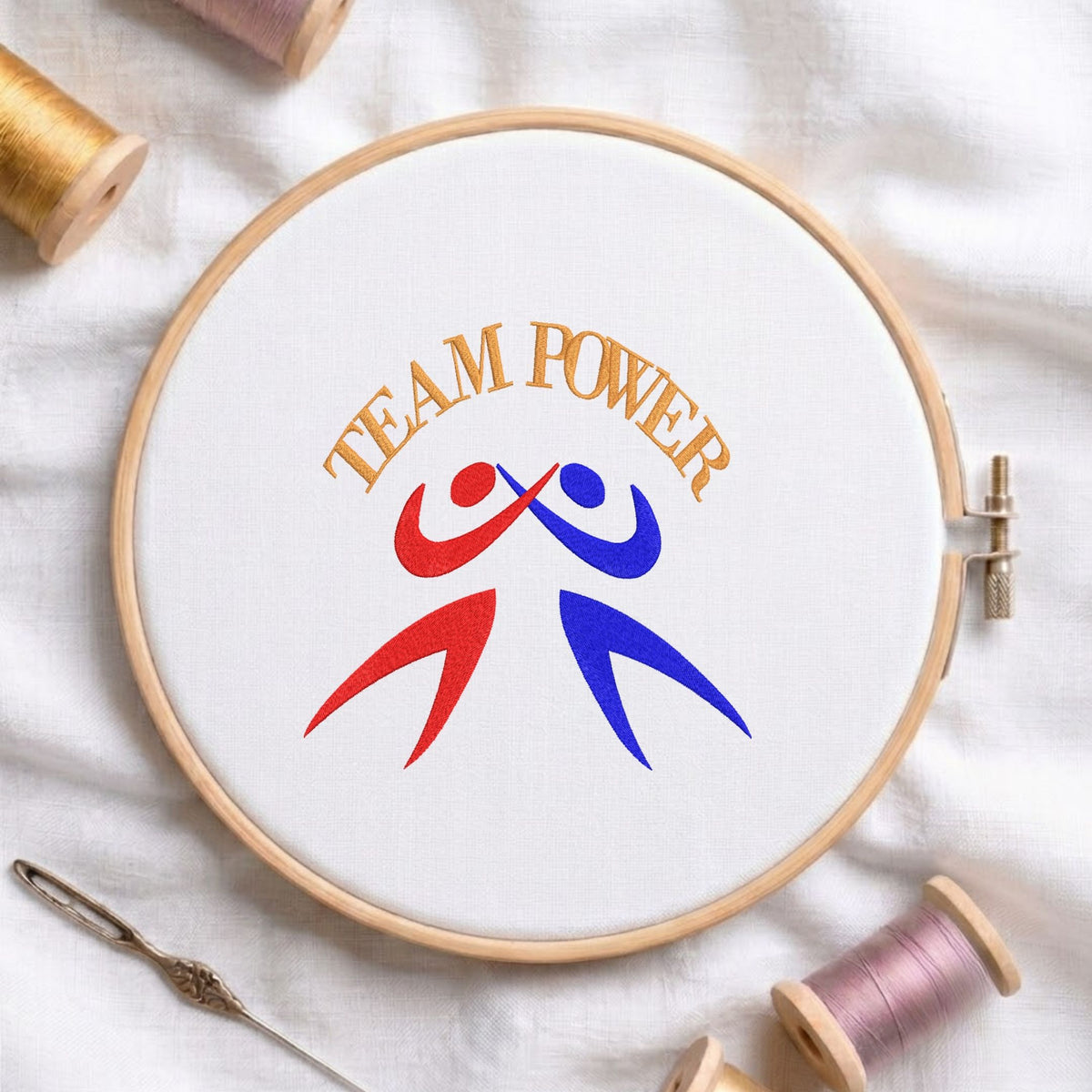 "Team Power" figures machine embroidery design displayed in a wooden hoop on white fabric with thread spools and a needle