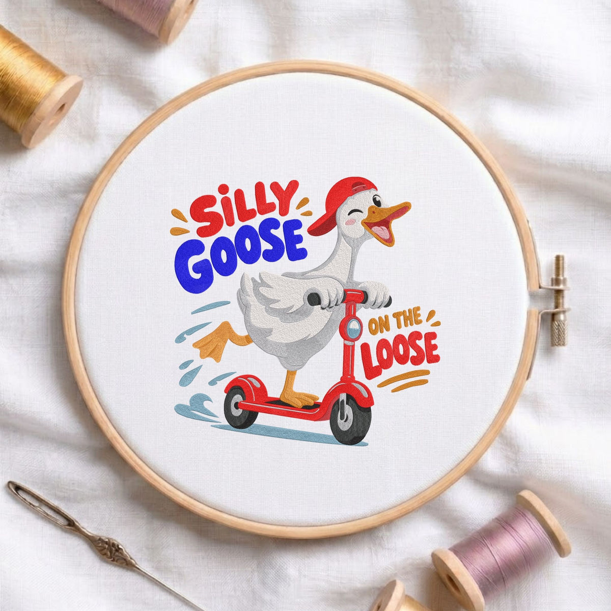  "Silly Goose on the Loose" funny cartoon duck wearing a red baseball cap and riding a red scooter machine embroidery design shown in a wooden embroidery hoop on white fabric with thread spools and a needle   