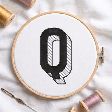 An embroidered 3D block letter "Q" with striped shading texture, stitched inside a wooden hoop on white fabric with sewing threads