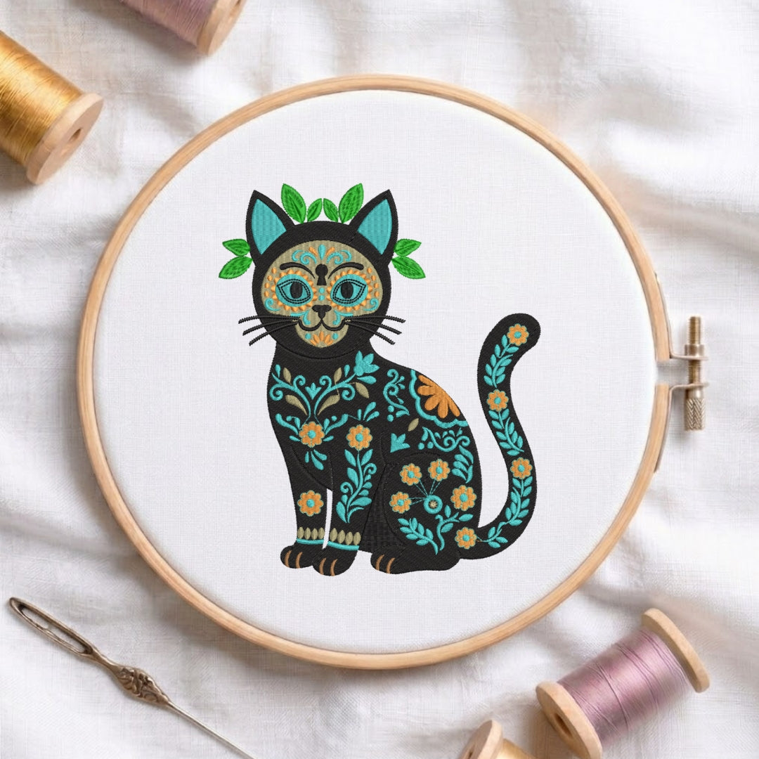 A wooden embroidery hoop on white fabric, featuring a stylized black cat with colorful floral patterns and a green leafy crown. Spools of thread and a needle are arranged around the hoop.