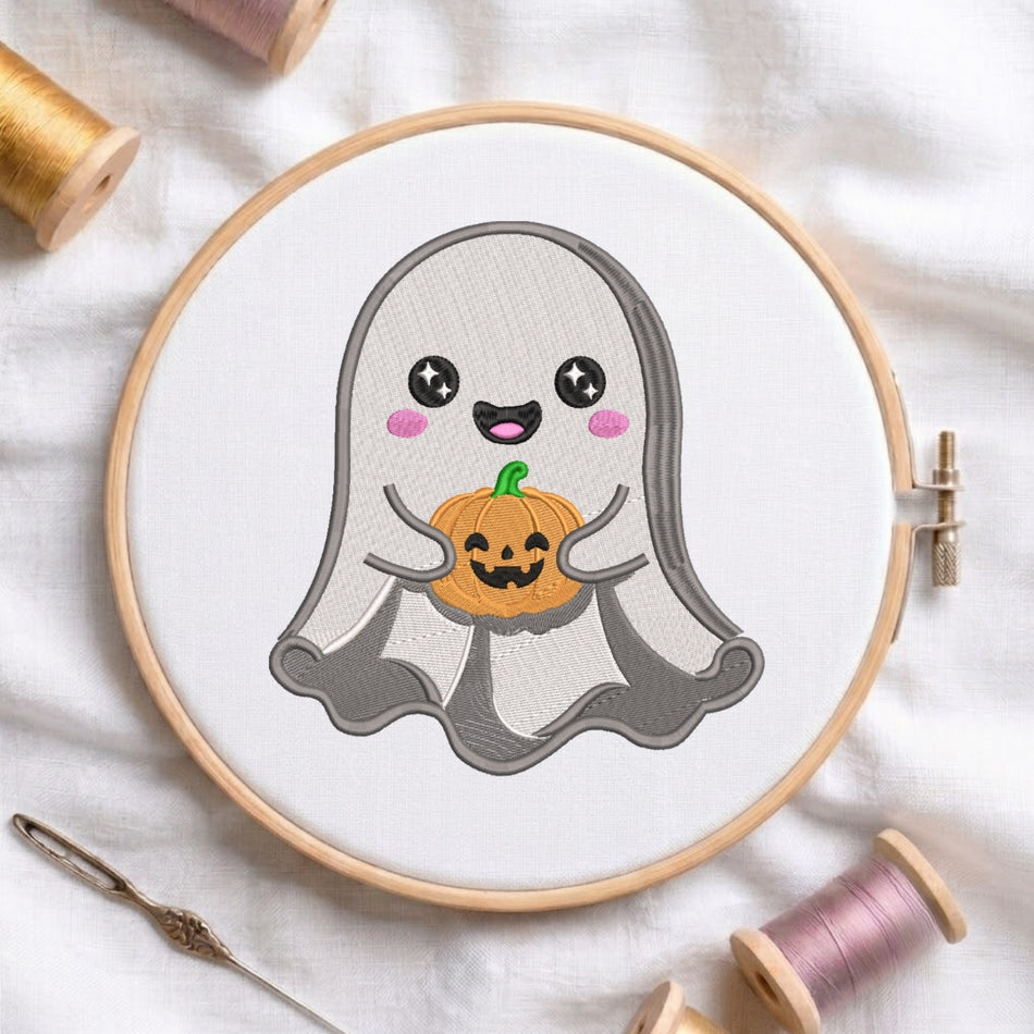 A circular embroidery hoop holding white fabric with a cute ghost design holding a small orange pumpkin. The hoop is styled on a white fabric background with spools of thread and a needle nearby.