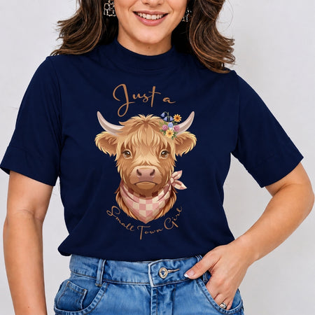A woman wearing a navy blue short-sleeve t-shirt with a graphic of a Highland cow and the text 'Just a Small Town Girl' in gold, paired with blue jeans.