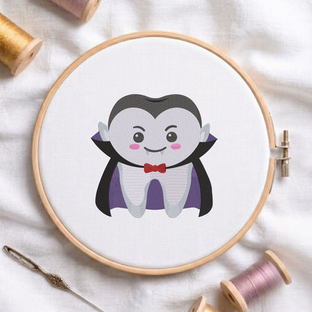 Cute vampire tooth Halloween dental machine embroidery design shown in a wooden embroidery hoop on white fabric with thread spools and a needle   