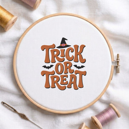 Trick or Treat" retro typography featuring a witch hat and bats machine embroidery design shown in a wooden embroidery hoop on white fabric with thread spools and a needle