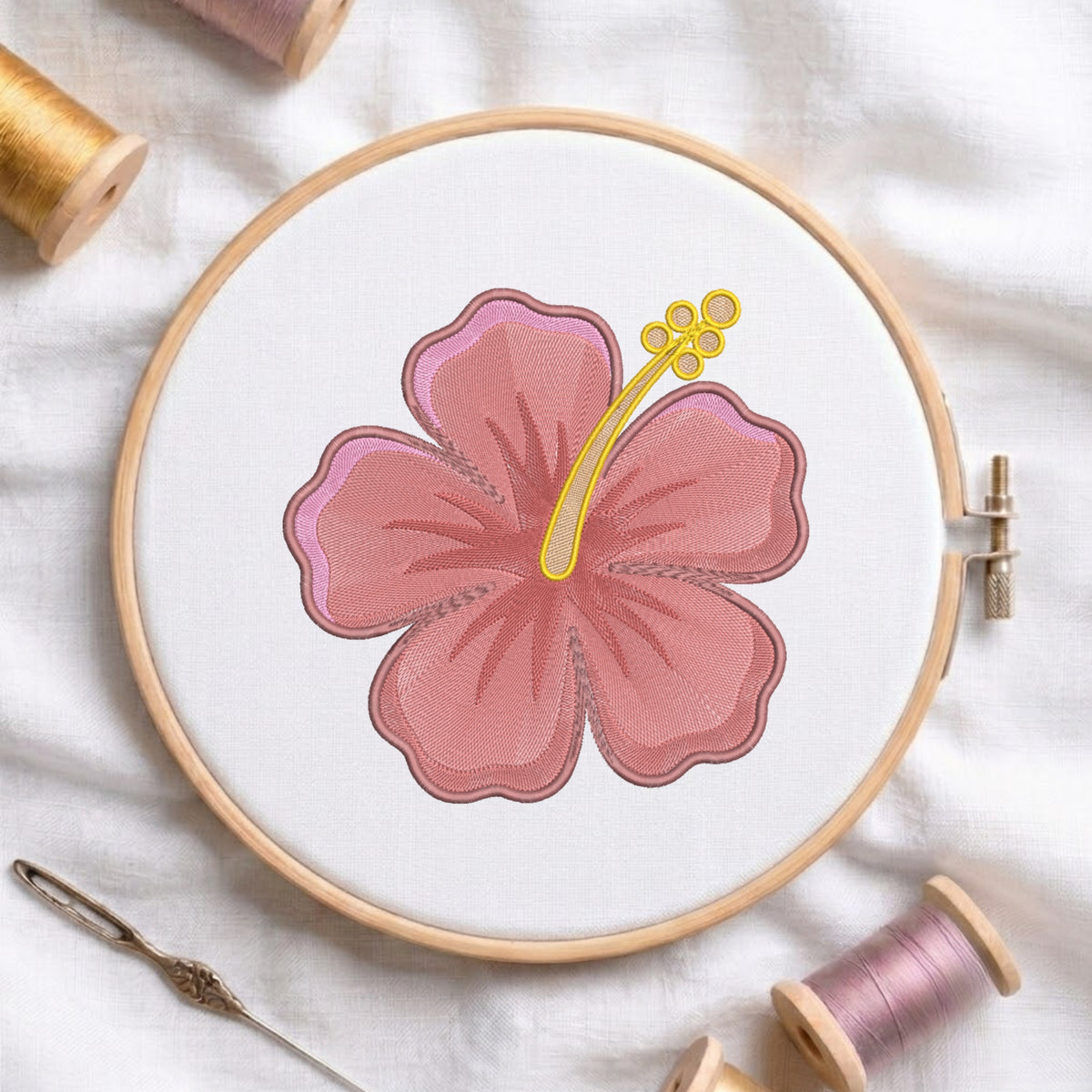 Pink hibiscus flower machine embroidery design framed in a wooden hoop with thread spools.