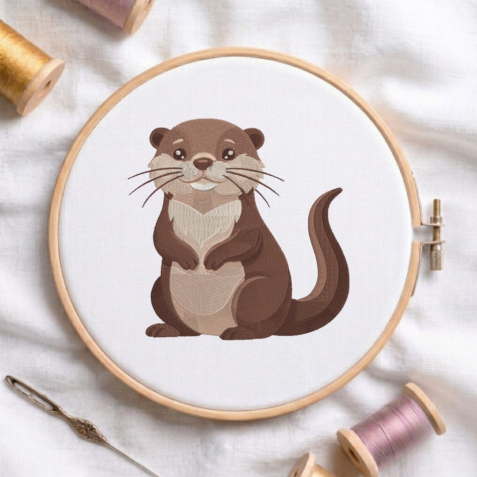 A wooden embroidery hoop holding white fabric with a cartoon-style brown and beige otter illustration. The hoop is photographed on a white fabric surface with spools of thread and a needle around it.