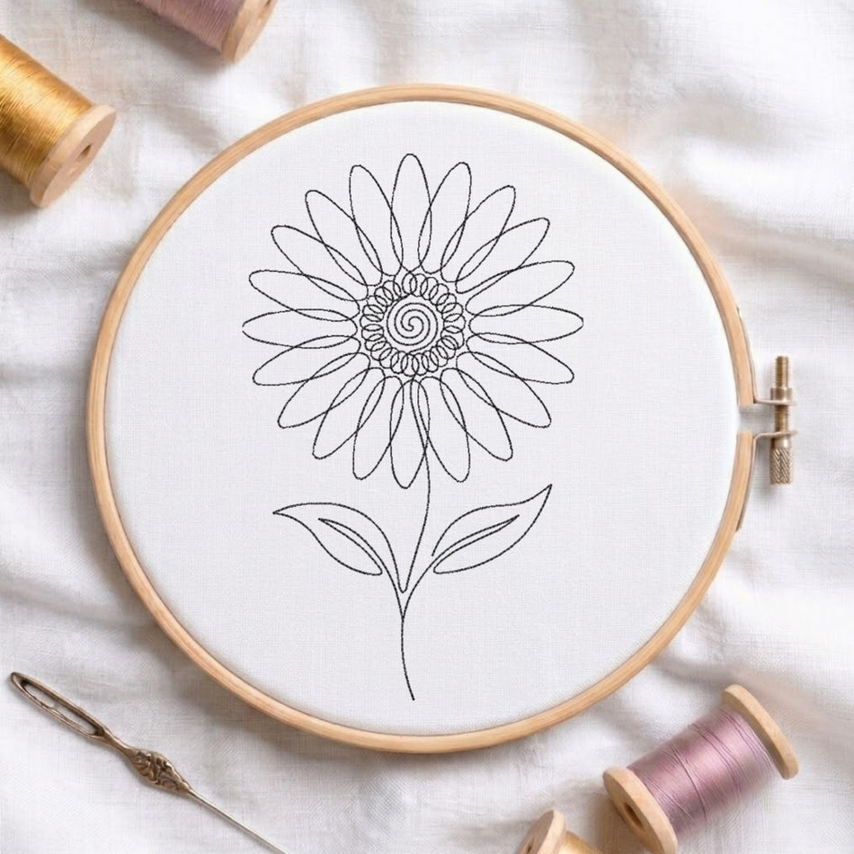 A circular embroidery hoop holding white fabric with a simple black line drawing of a flower. The hoop is styled on a white fabric surface with spools of thread and a needle around it.