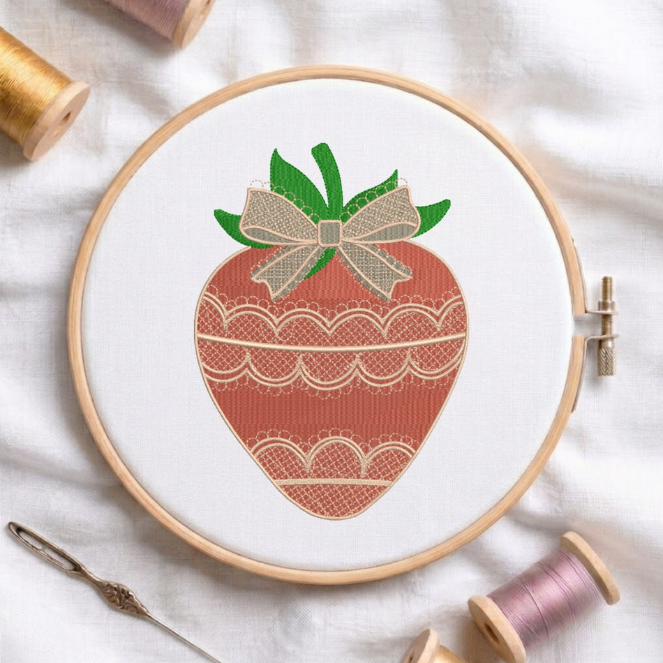 A strawberry-themed embroidery design displayed inside a wooden embroidery hoop on white fabric, surrounded by spools of thread and a needle.
