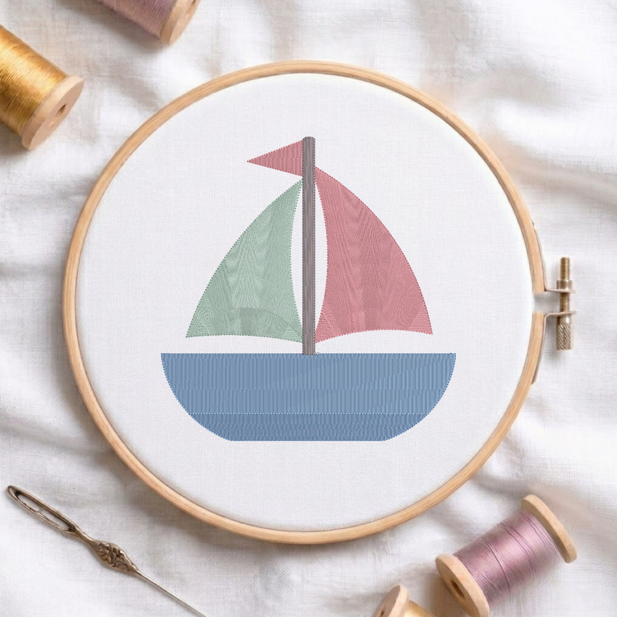 An embroidered colorful sailboat design with a blue hull, green and pink sails stitched inside a wooden hoop on white fabric with sewing threads.