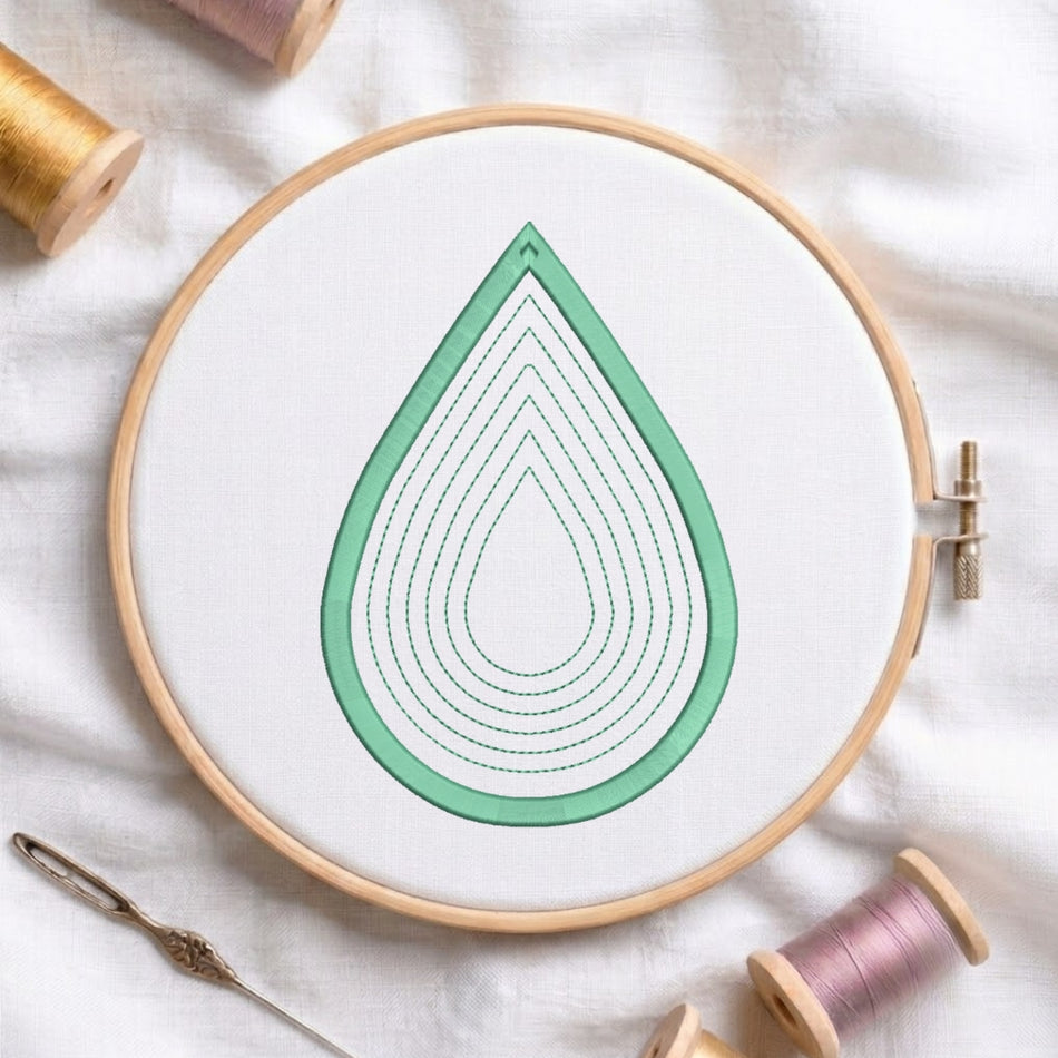 A wooden embroidery hoop holding white fabric with a mint green teardrop design outlined in stitched concentric loops. A needle lies at the lower left, and spools of thread are visible around the hoop on a white fabric background.