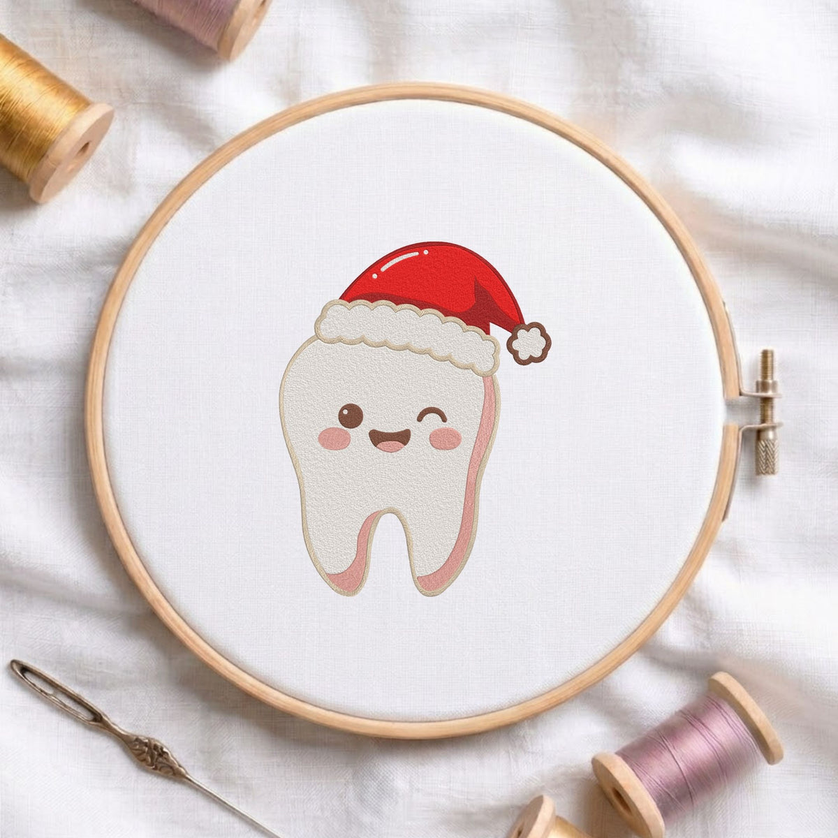 Cute winking tooth wearing a red Santa hat Christmas dental machine embroidery design shown in a wooden embroidery hoop on white fabric with thread spools and a needle   