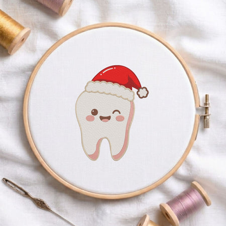 Cute winking tooth wearing a red Santa hat Christmas dental machine embroidery design shown in a wooden embroidery hoop on white fabric with thread spools and a needle   