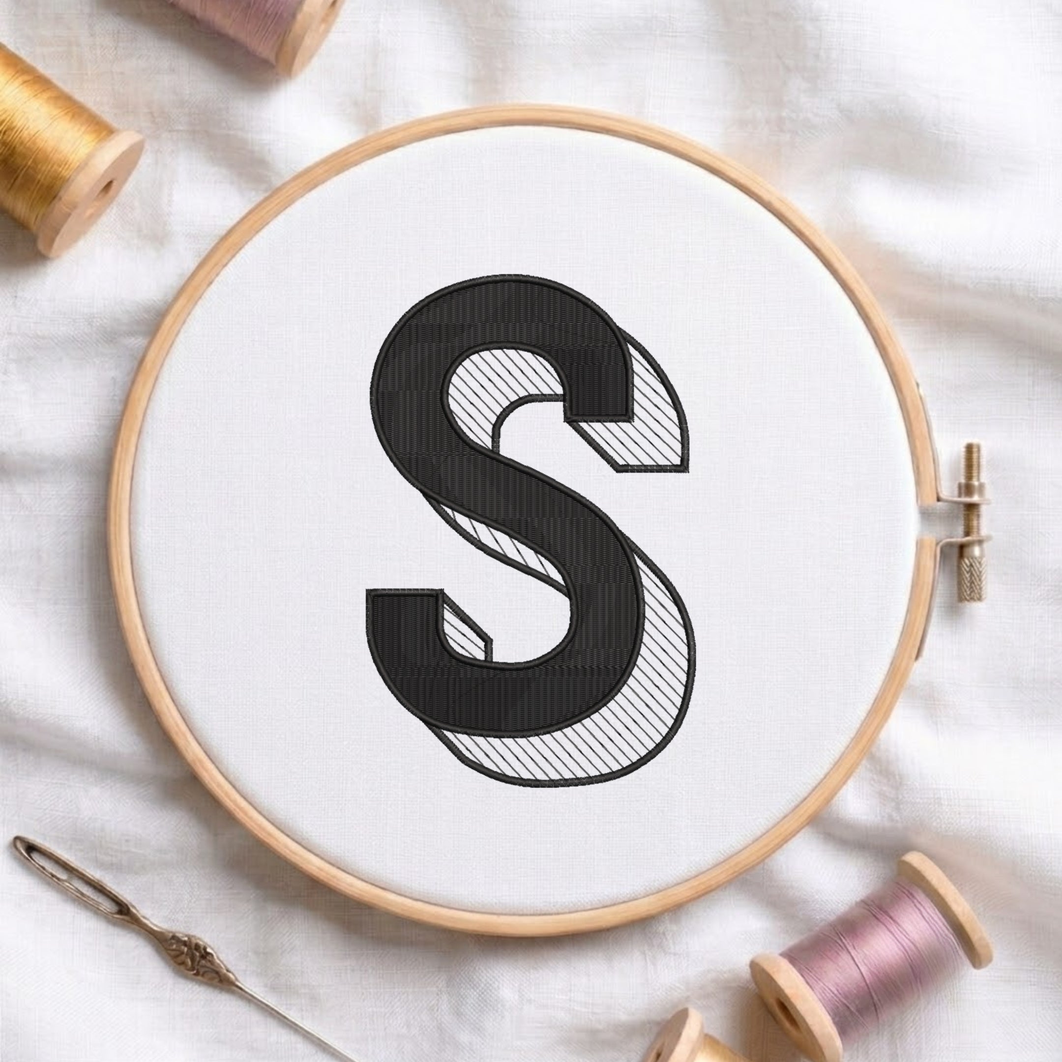 An embroidered 3D block letter "S" with striped shading texture, stitched inside a wooden hoop on white fabric with sewing threads.