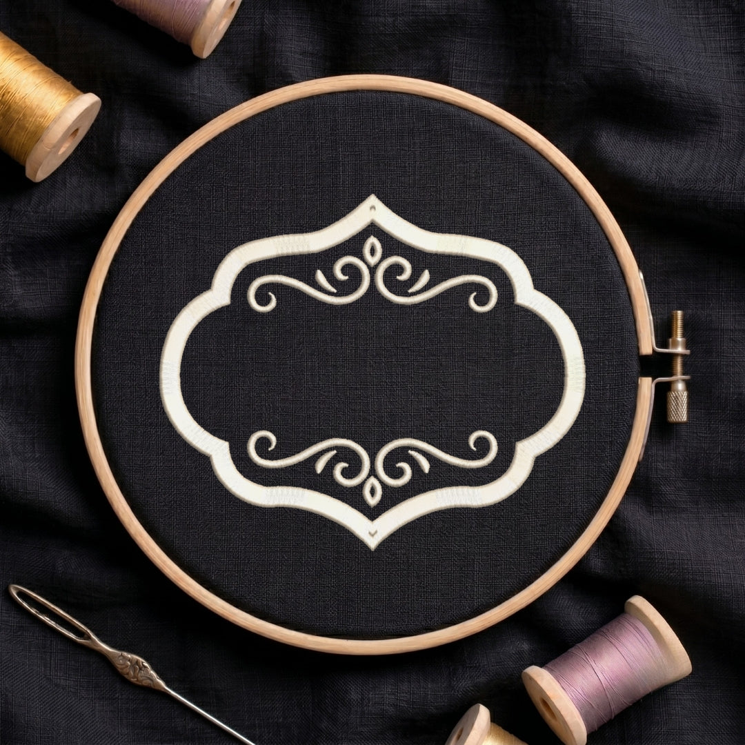 A wooden embroidery hoop holding black fabric with a white ornamental scroll design, surrounded by spools of thread and a needle on a dark fabric background.