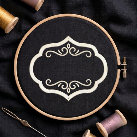 A wooden embroidery hoop holding black fabric with a white ornamental scroll design, surrounded by spools of thread and a needle on a dark fabric background.