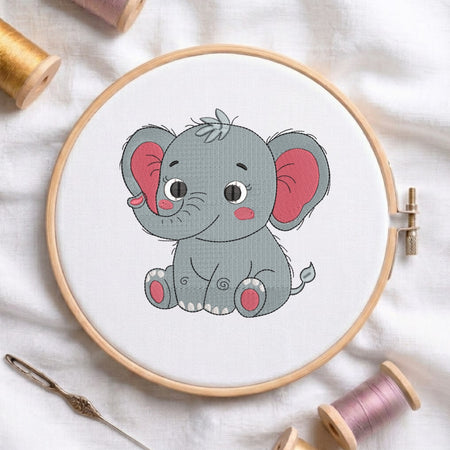 A circular embroidery hoop holding white fabric with a cartoon gray elephant design, surrounded by spools of thread and a needle on a white fabric background.