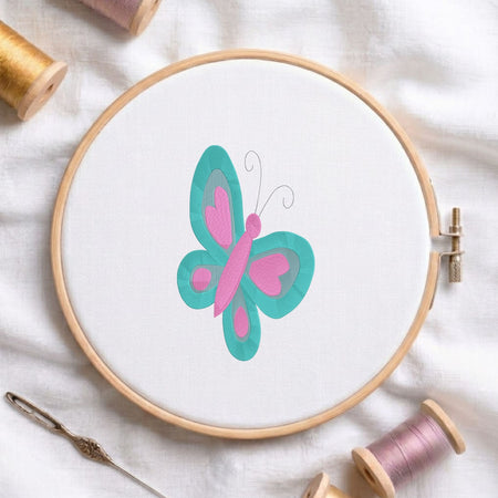 Green and yellow butterfly machine embroidery design displayed in a wooden embroidery hoop on white fabric with thread spools and a needle