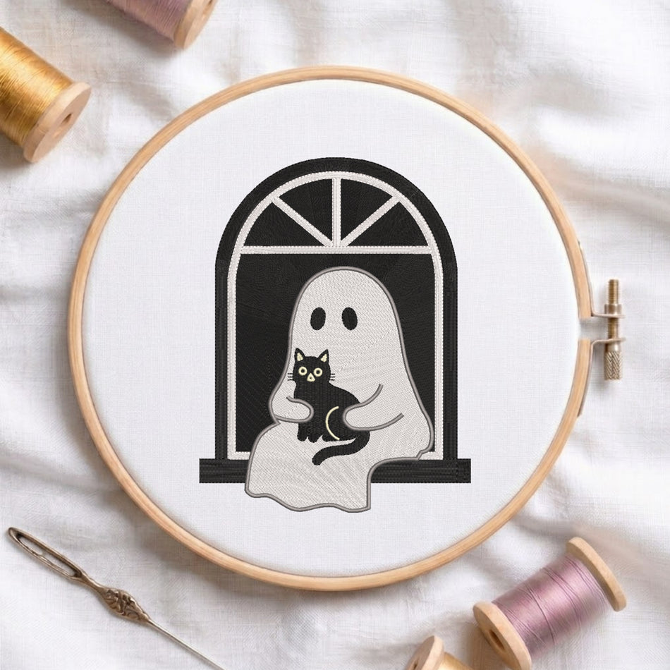 A circular embroidery hoop on white fabric, showing a black-and-white ghost holding a black cat design. Spools of thread and a needle are arranged around it.