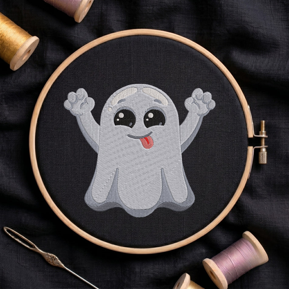 A circular embroidery hoop holding a stitched cartoon ghost design on black fabric, surrounded by spools of thread and a needle on a dark cloth background.
