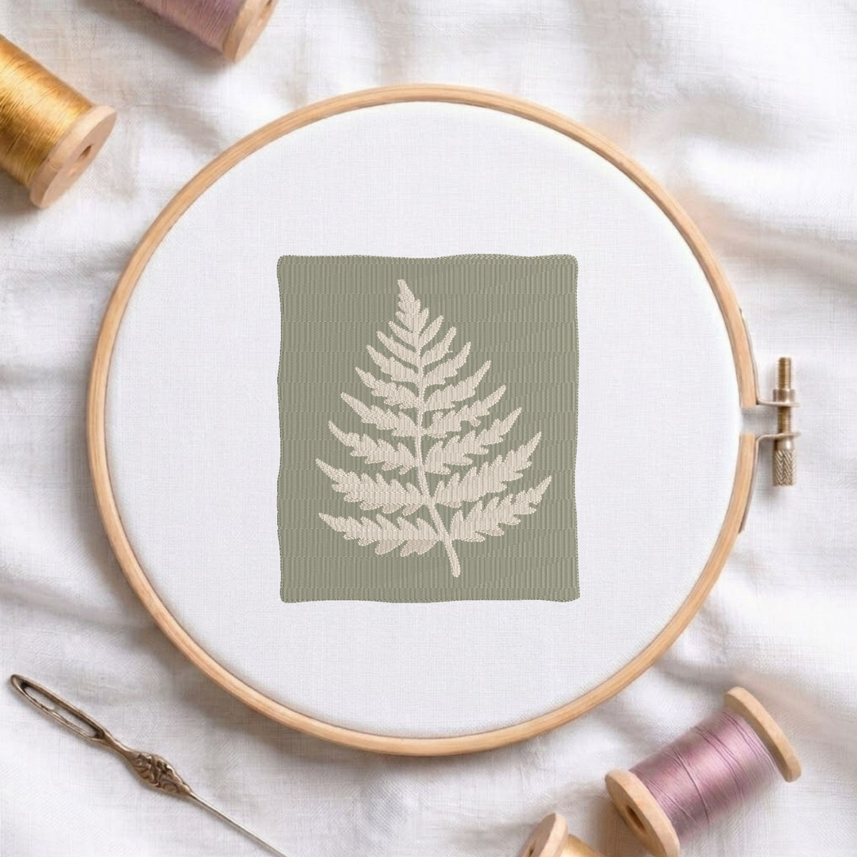 Vintage botanical rosehip branch machine embroidery design framed inside a rounded rectangular border, displayed in a wooden hoop on white fabric with thread spools and a needle