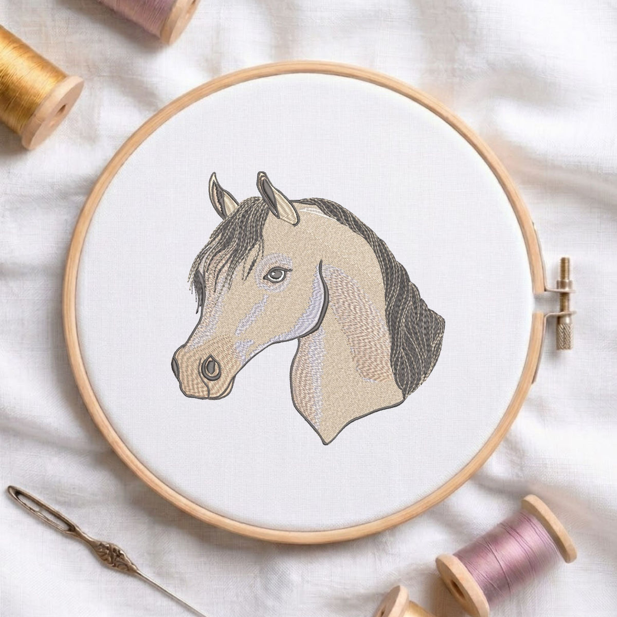 Elegant horse head machine embroidery design displayed in a wooden hoop on white fabric with thread spools and a needle