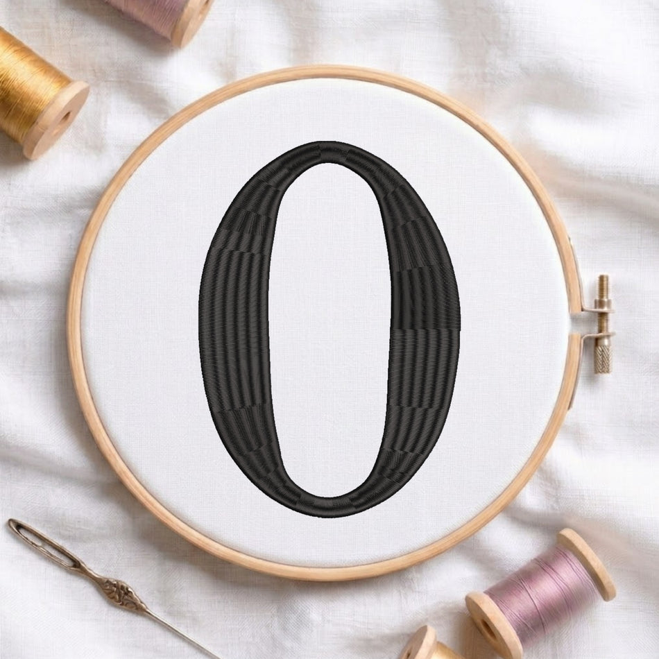 A large embroidered black letter zero inside a light wood embroidery hoop, set on a white fabric background with spools of thread and a needle nearby.