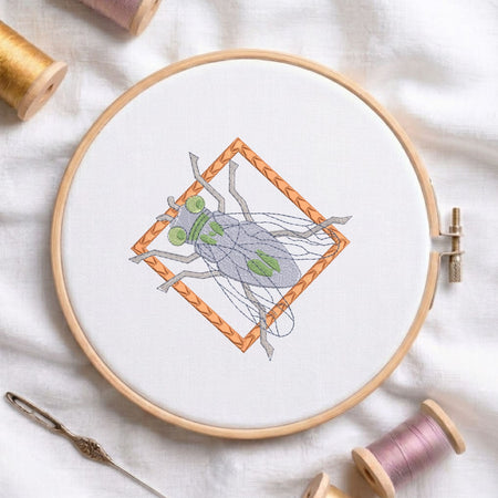  Cicada bug insect framed machine embroidery design displayed in a wooden hoop on white fabric with thread spools and a needle   