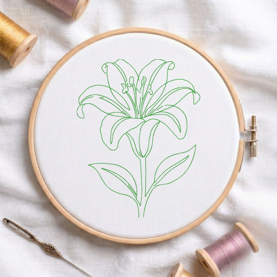 A wooden embroidery hoop holding white fabric with a green outline drawing of a lily flower. Spools of thread and a needle are arranged around it on a white fabric background.