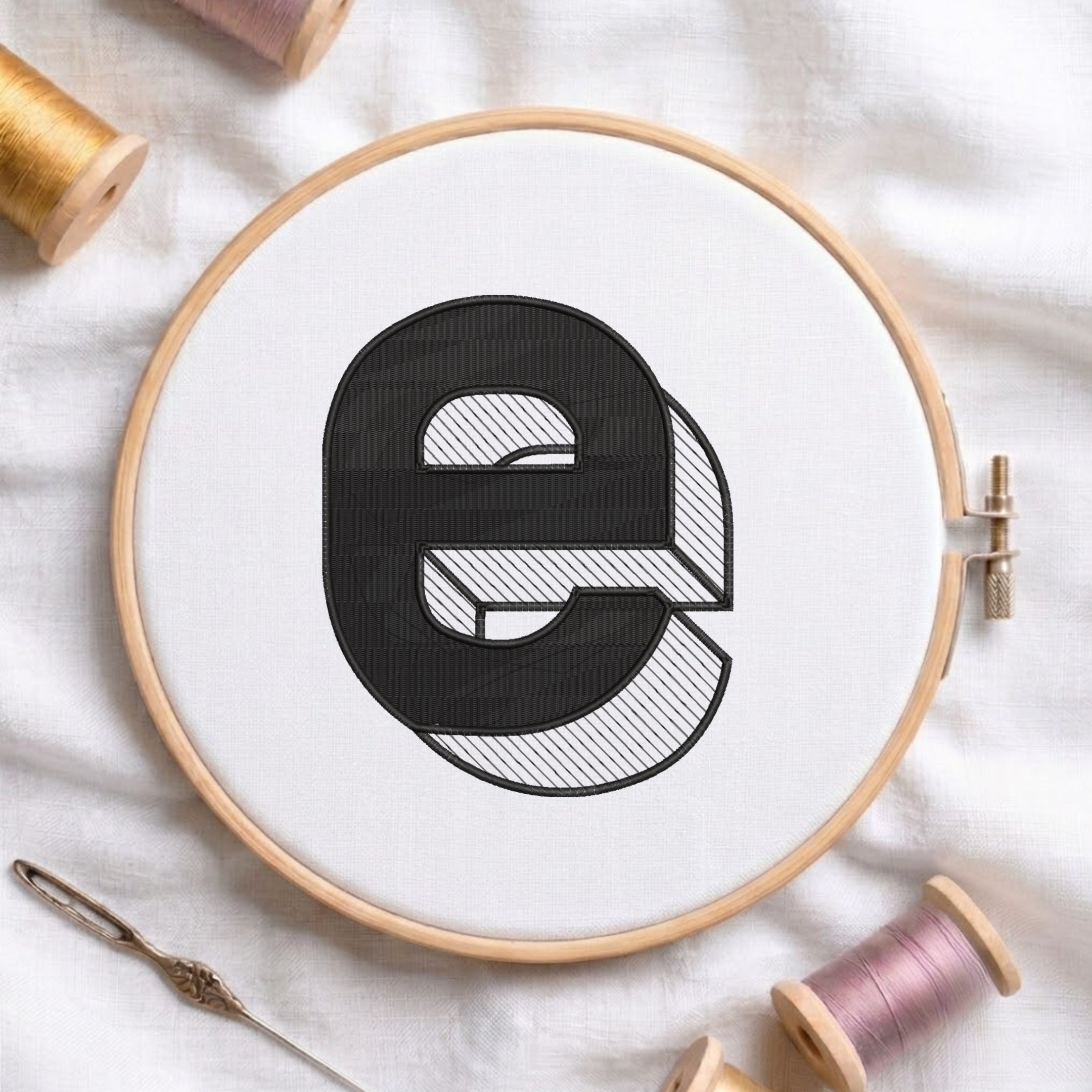 An embroidered 3D block lowercase letter "e" with striped shading texture, stitched inside a wooden hoop on white fabric with sewing threads.