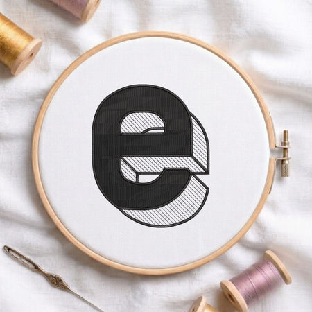 An embroidered 3D block lowercase letter "e" with striped shading texture, stitched inside a wooden hoop on white fabric with sewing threads.