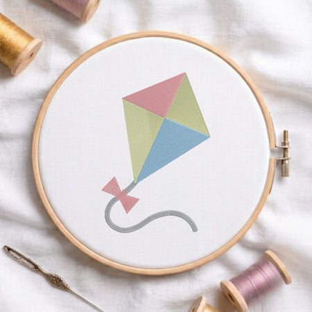 An embroidered colorful kite design with pink, yellow, and blue panels stitched inside a wooden hoop on white fabric with sewing threads.