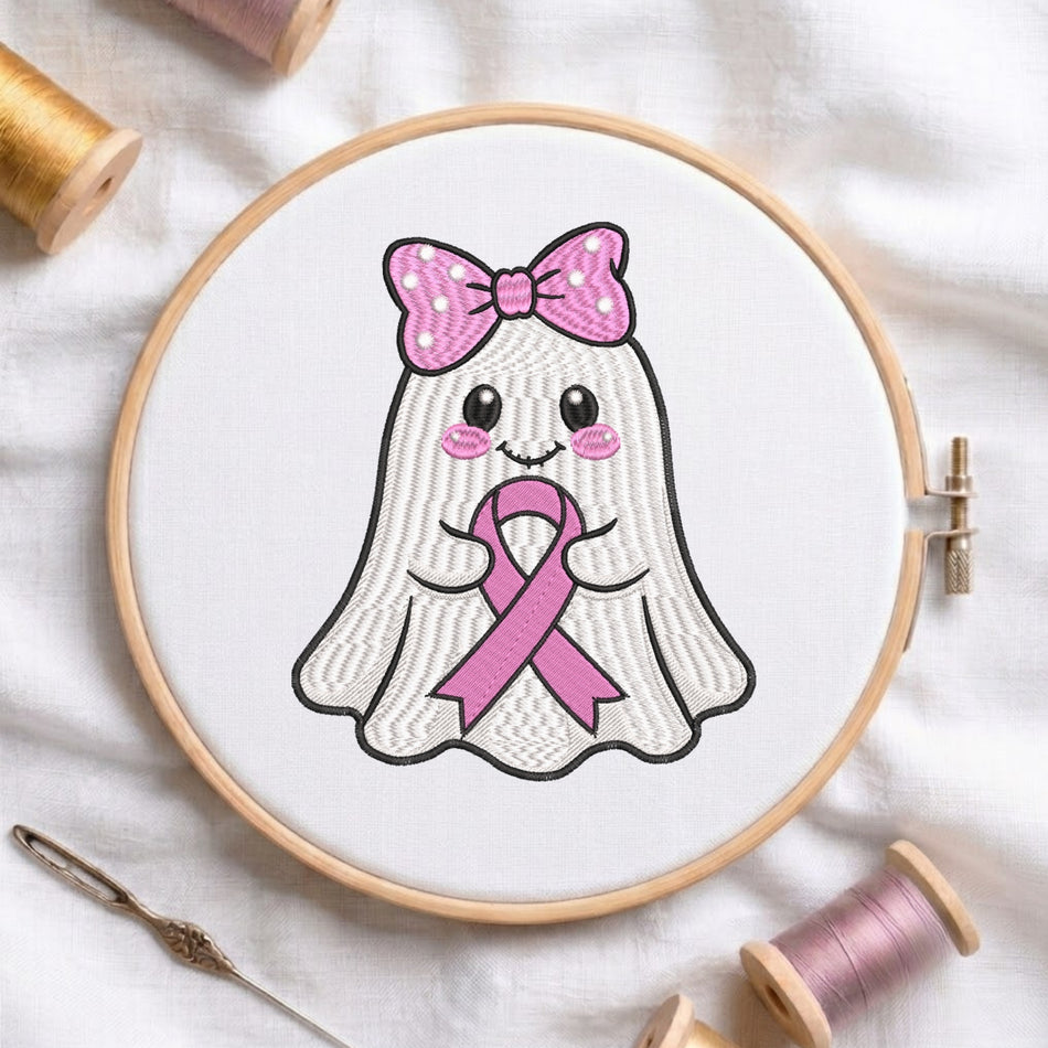 A wooden embroidery hoop holds a white fabric panel with a cute embroidered ghost design wearing a pink polka-dot bow and holding a pink ribbon. The hoop is photographed on a white fabric surface with spools of thread and a needle around it.