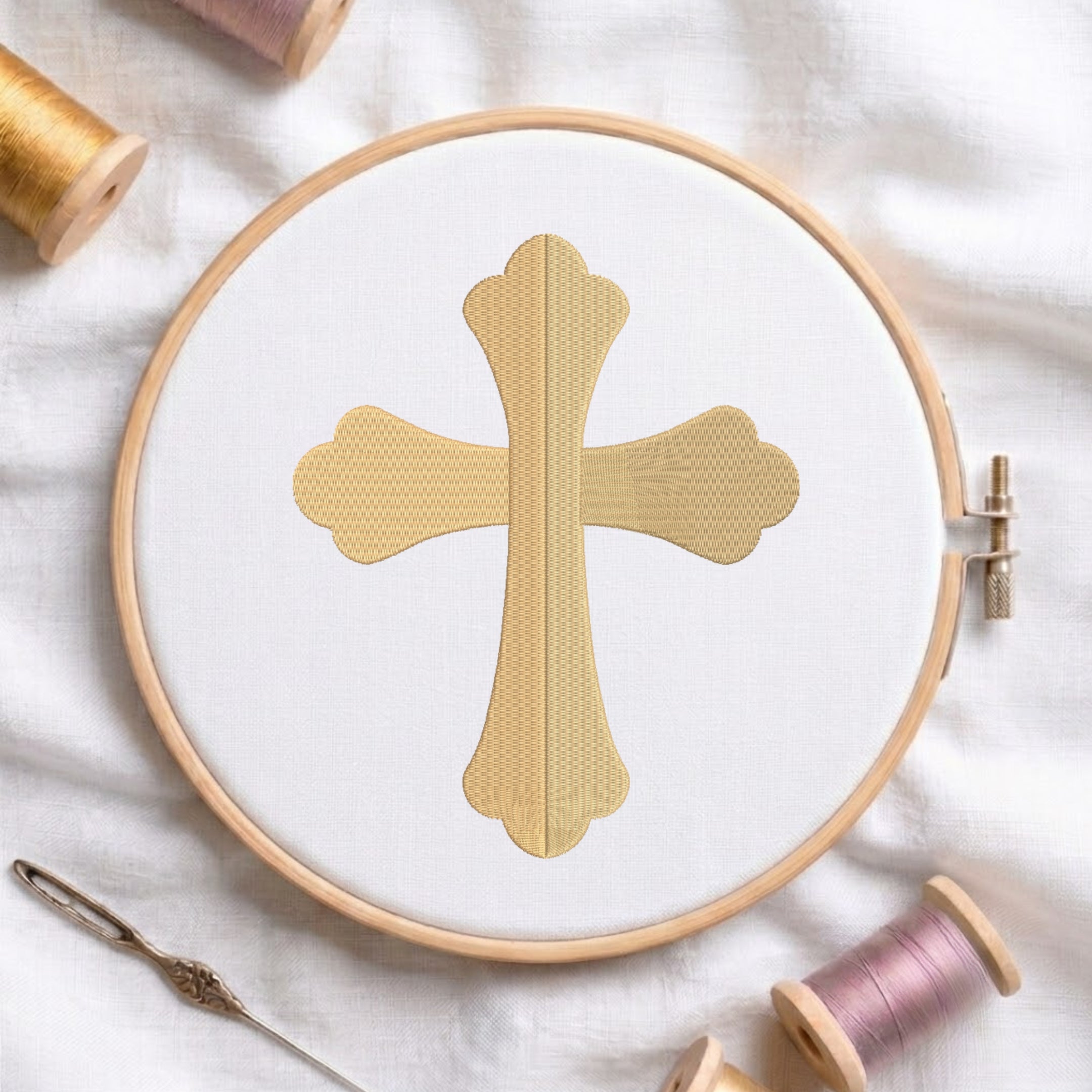 Solid gold flared cross embroidered on white fabric inside a wooden hoop.