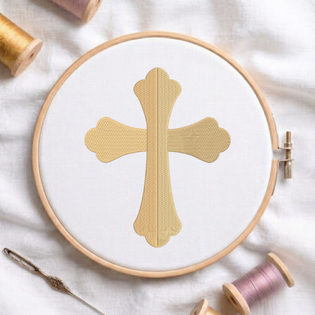 Solid gold flared cross embroidered on white fabric inside a wooden hoop.