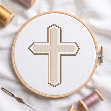 An embroidery hoop on a white cloth displays a finished embroidery design of a textured beige Christian cross with a brown outline, flanked by spools of thread and a needle.