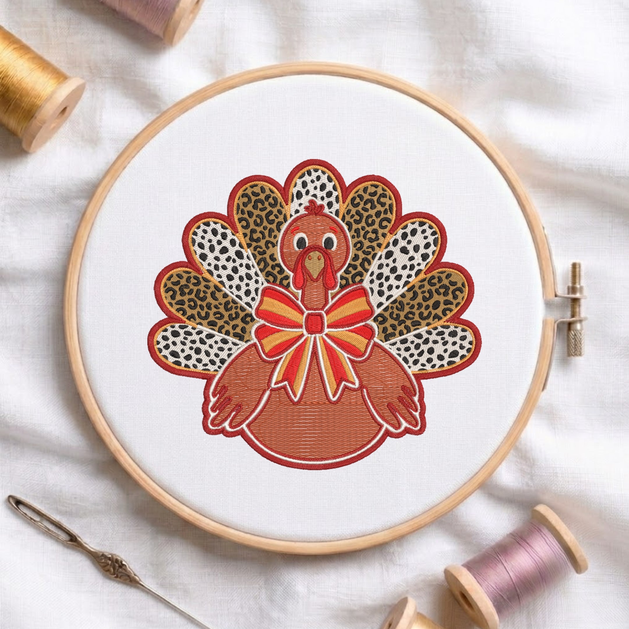 A circular embroidery hoop holding white fabric with a colorful turkey design. The turkey has leopard-print and white patterned feathers, a red wattle, and a red-and-yellow bow.