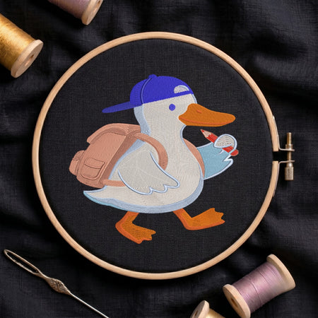 A circular embroidery hoop holds a stitched duck character wearing a blue cap and carrying a pink backpack, surrounded by spools of thread and a needle on a dark fabric background.