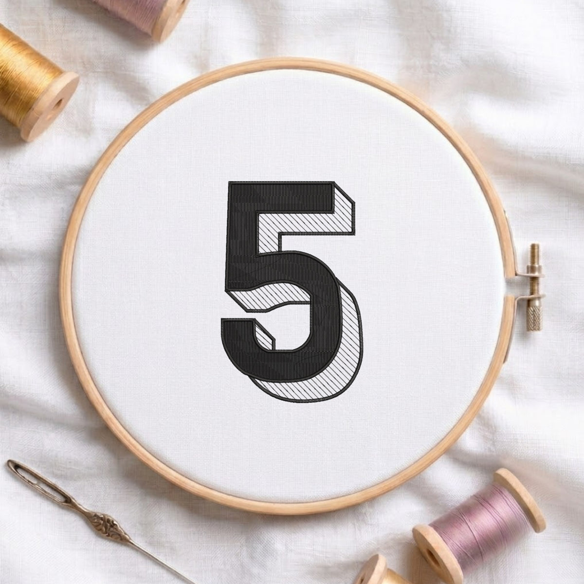 An embroidered 3D block number "5" with striped shading texture, stitched inside a wooden hoop on white fabric with sewing threads.
