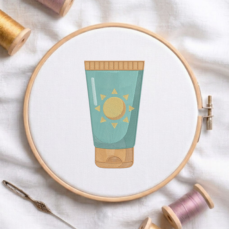 A circular embroidery hoop on white fabric holds a stylized embroidered tube illustration in teal and gold. Surrounding props include spools of thread and a needle on a soft white textile background.