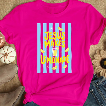 Pink t-shirt with 'Jesus Makes Lemonade' text and graphics on a textured surface.
