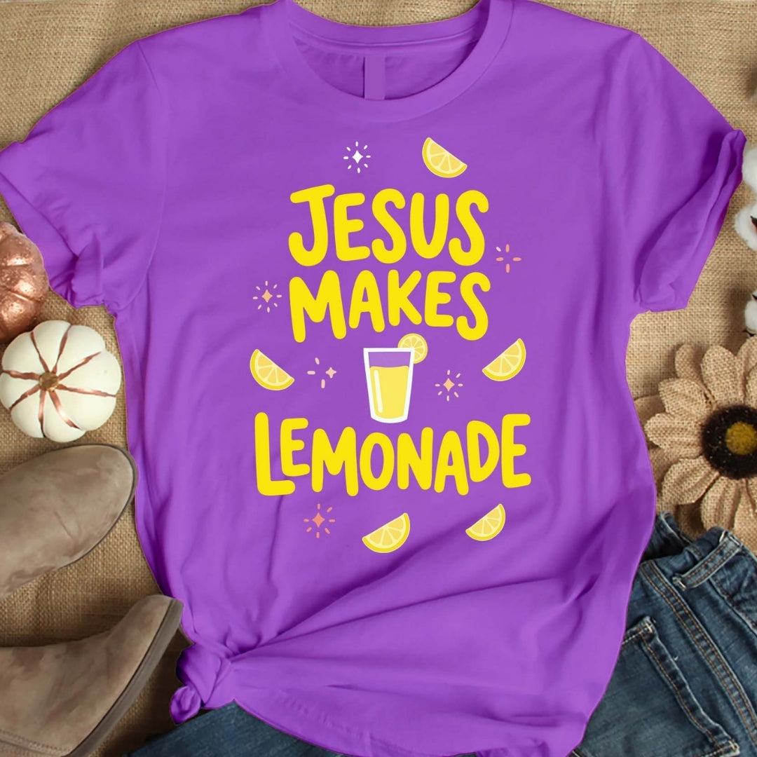 Purple t-shirt with yellow 'Jesus Makes Lemonade' text and graphics on a textured surface.