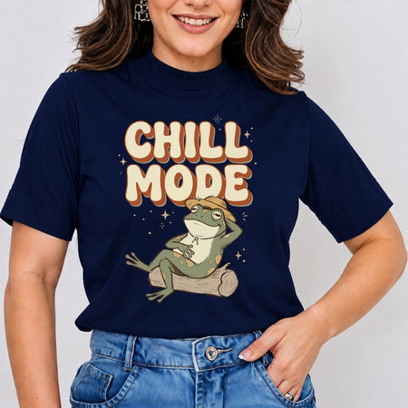 A woman wearing a navy blue graphic t-shirt with a cartoon frog sitting on a log under the words 'CHILL MODE' in cream and orange lettering, paired with blue jeans.