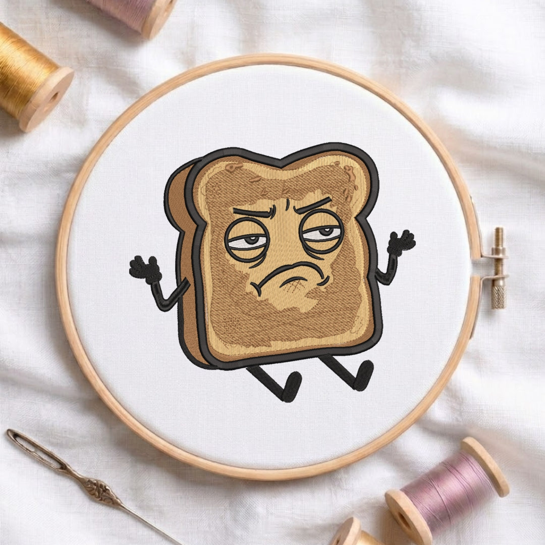 A circular embroidery hoop on white fabric, featuring a cartoon graphic of a grumpy slice of toast with arms and legs. Spools of thread and a needle are arranged around it.