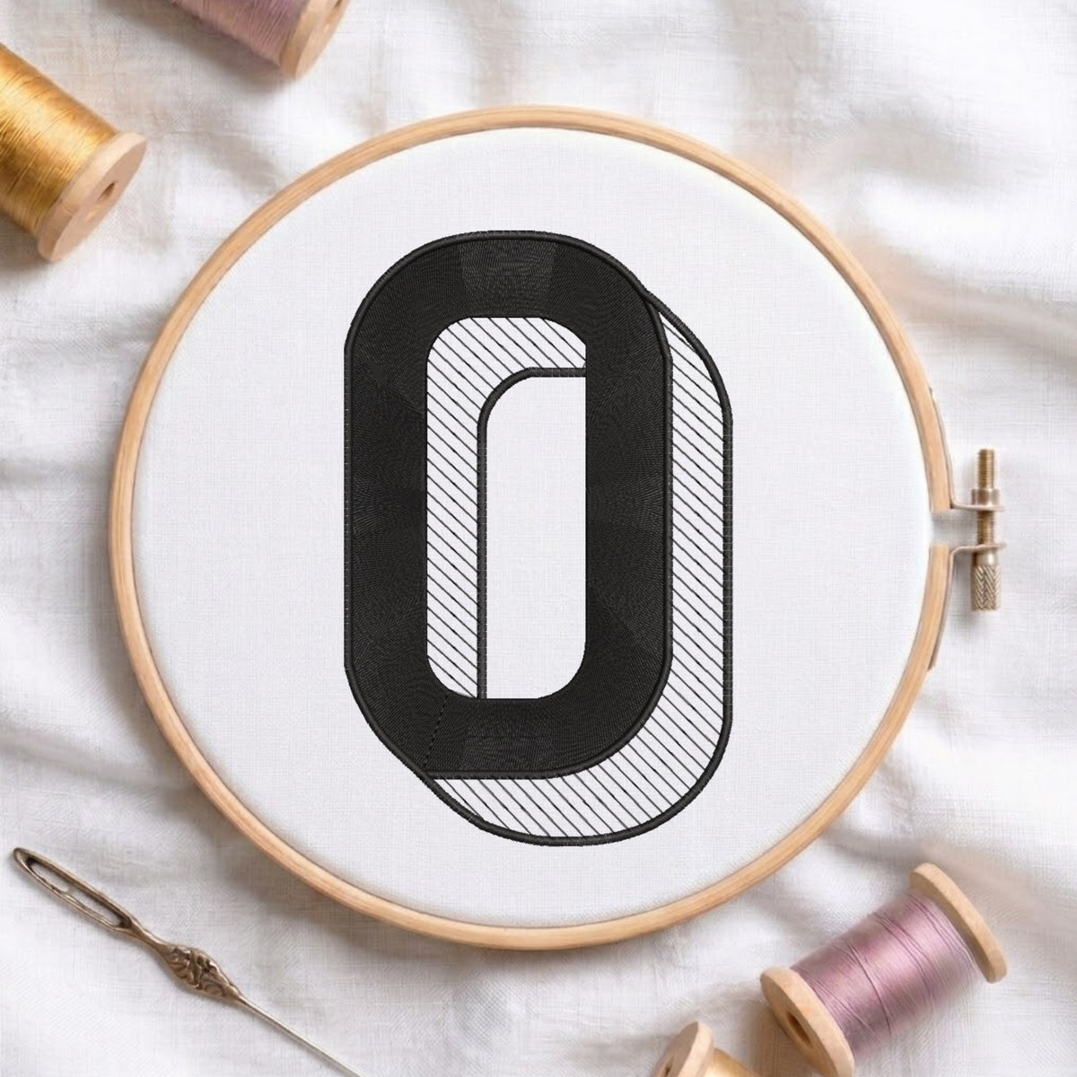 An embroidered 3D block letter "O" with striped shading texture, stitched inside a wooden hoop on white fabric with sewing threads.