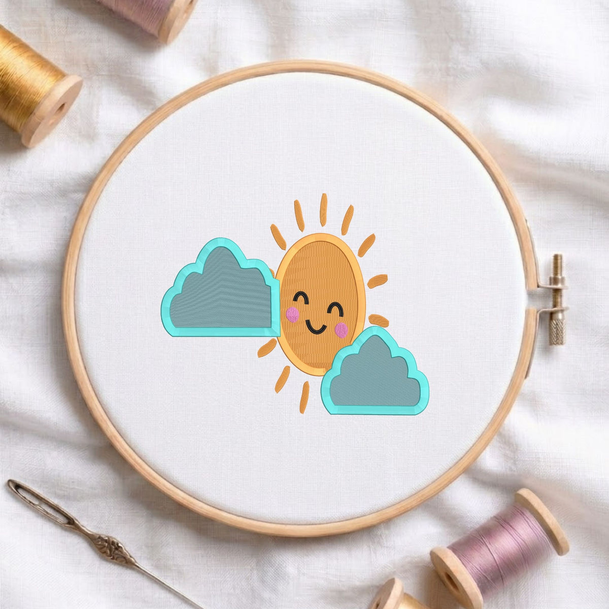 Cute smiling sun with blue clouds machine embroidery design displayed in a wooden embroidery hoop on white fabric with thread spools and a needle