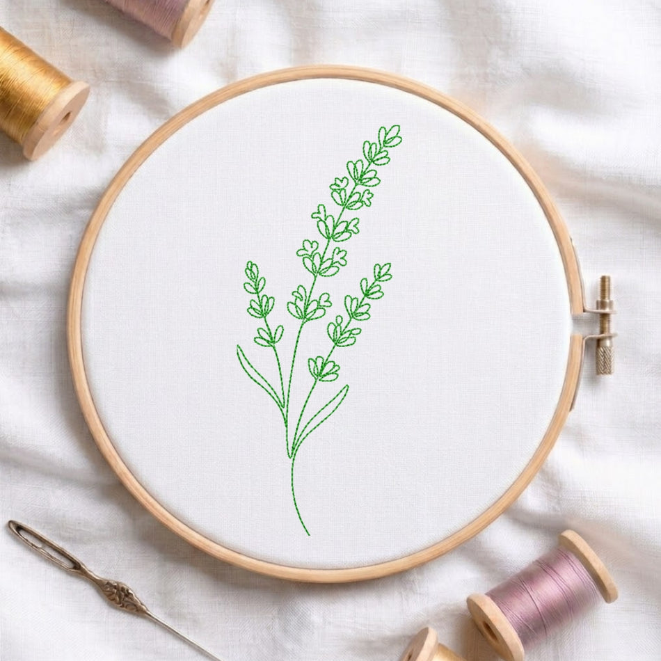 The green, line-art embroidered lavender design secured in a wooden embroidery hoop, displayed with embroidery thread spools and a needle on a white fabric background.
