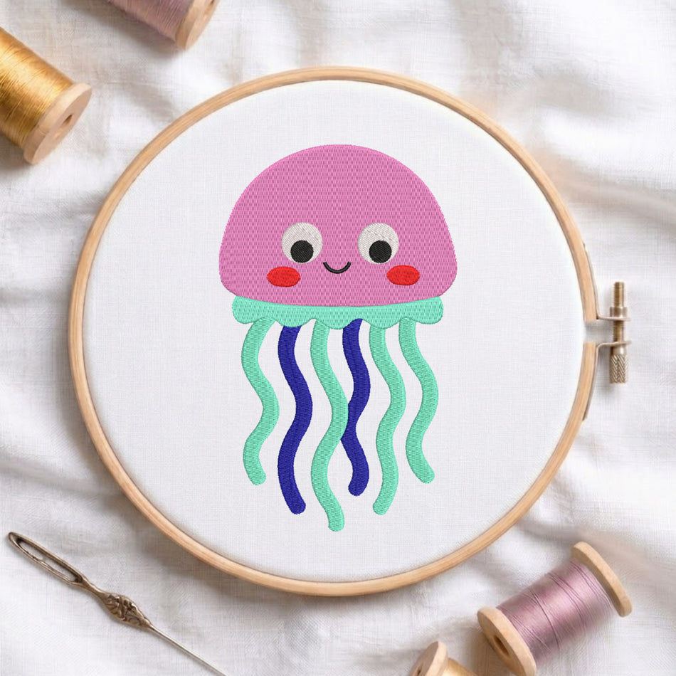 A wooden embroidery hoop holding white fabric with a colorful cartoon jellyfish design. The jellyfish has a pink dome head, white eyes, red cheeks, and wavy mint green and blue tentacles.