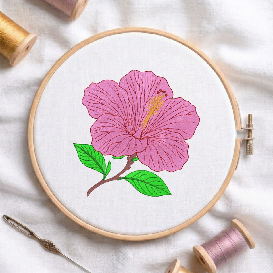 A circular embroidery hoop holding white fabric with a pink hibiscus flower and green leaves stitched in the center, surrounded by spools of thread and a needle on a white fabric background.